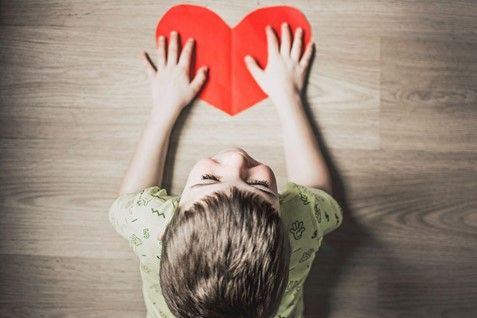 A boy is holding a paper heart on the floor