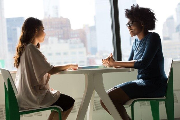 Two women sitting at a table talking to each other.